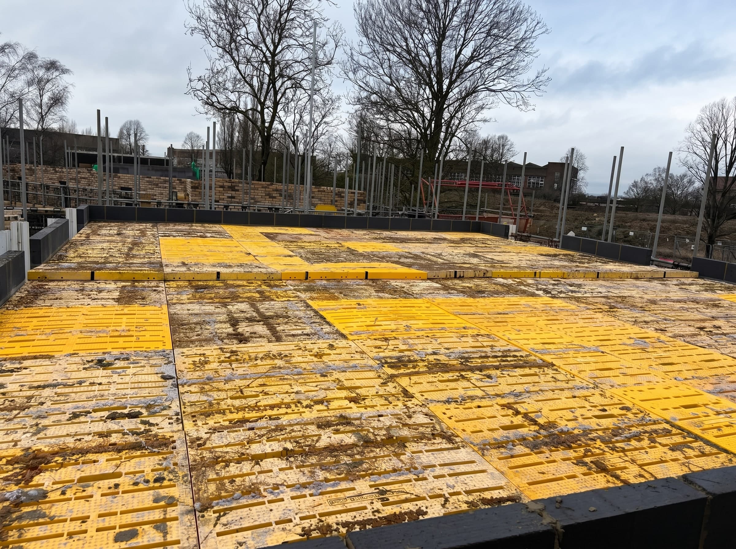 Yellow Trad Deck platform installed across a house plot, trees beyond